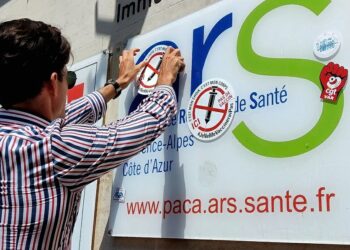 Un manifestant plaque un autocollant "non au vaccin" sur le logo de l'ARS Paca à Marseille lors d'une mobilisation anti-passe sanitaire